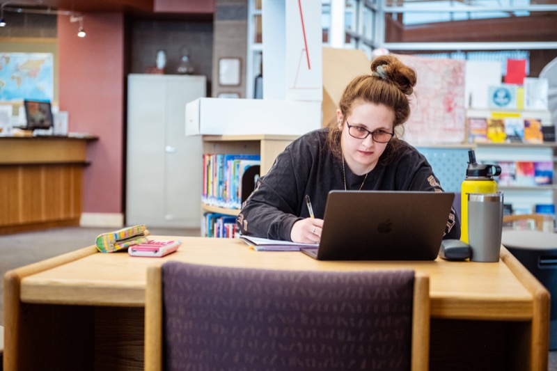 Student studying with a laptop and notebook in the campus library