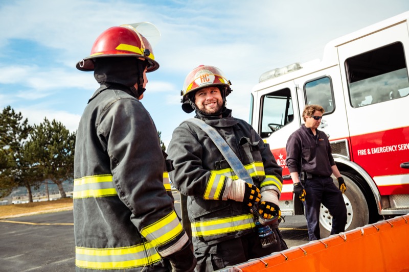 Two firefighters in turnout gear beside a Fire and Emergency Services engine